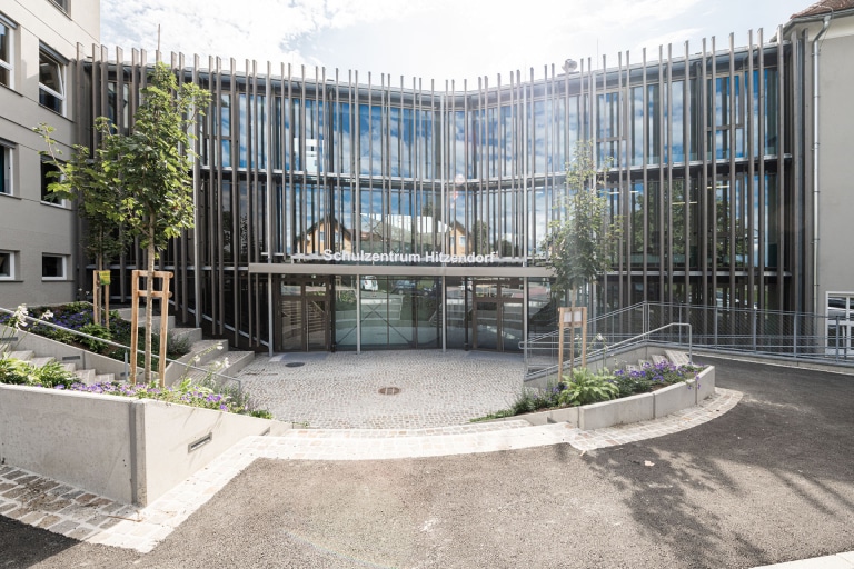 Hitzendorf-Schule-8524, Ansicht von Außen, Teilausschnitt Eingang für die Schüler und Schülerinnen von Hitzendorf, umgeben von Bäumen und Blumen, ARTiVO Hitzendorf-Schule-8524, Ansicht von Außen, Teilausschnitt Eingang für die Schüler und Schülerinnen von Hitzendorf, umgeben von Bäumen und Blumen, ARTiVO